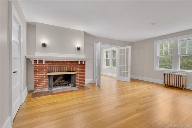219 Jordan Ln, Wethersfield, CT 06109 - unfurnished living room with radiator heating unit, hardwood / wood-style floors, a brick fireplace, and french doors