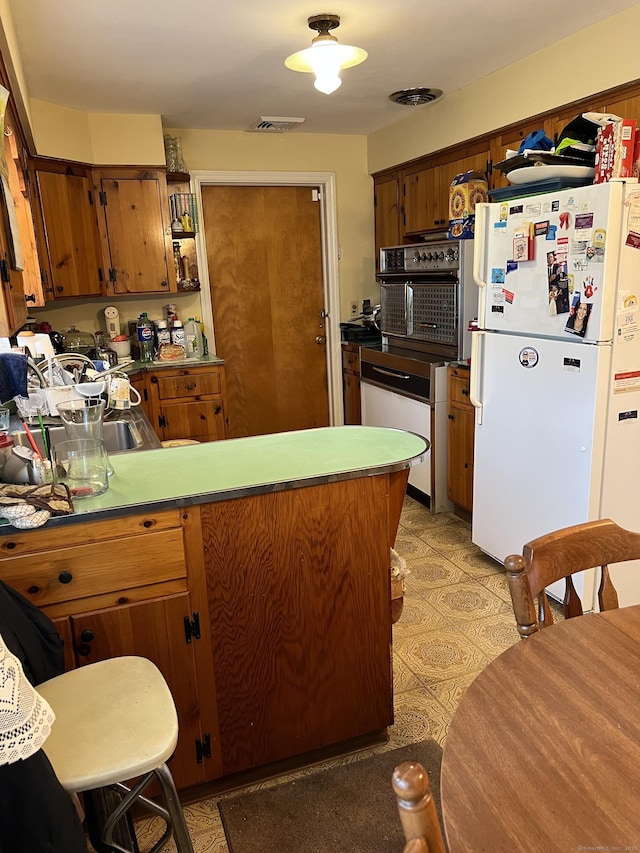 kitchen with freestanding refrigerator, a peninsula, and brown cabinetry