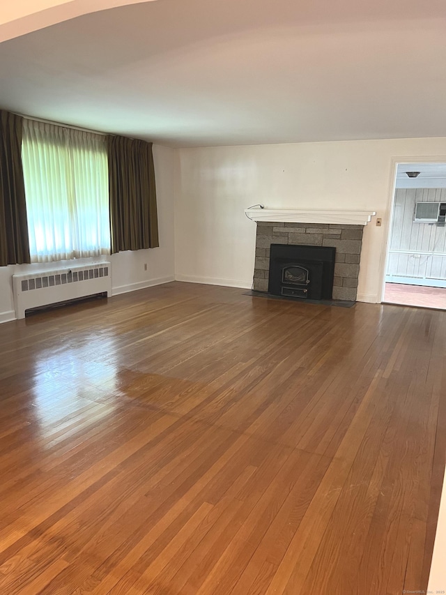 unfurnished living room featuring radiator heating unit, wood-type flooring, a fireplace, and a wall mounted air conditioner