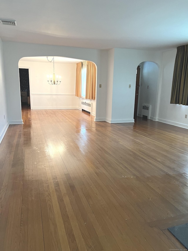 empty room with radiator heating unit, arched walkways, dark wood-style flooring, and a chandelier