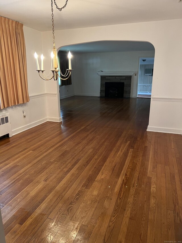 unfurnished living room with dark wood-style flooring, a chandelier, radiator heating unit, arched walkways, and a fireplace