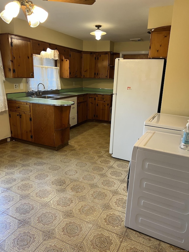 kitchen with freestanding refrigerator, a peninsula, light flooring, washing machine and clothes dryer, and brown cabinetry