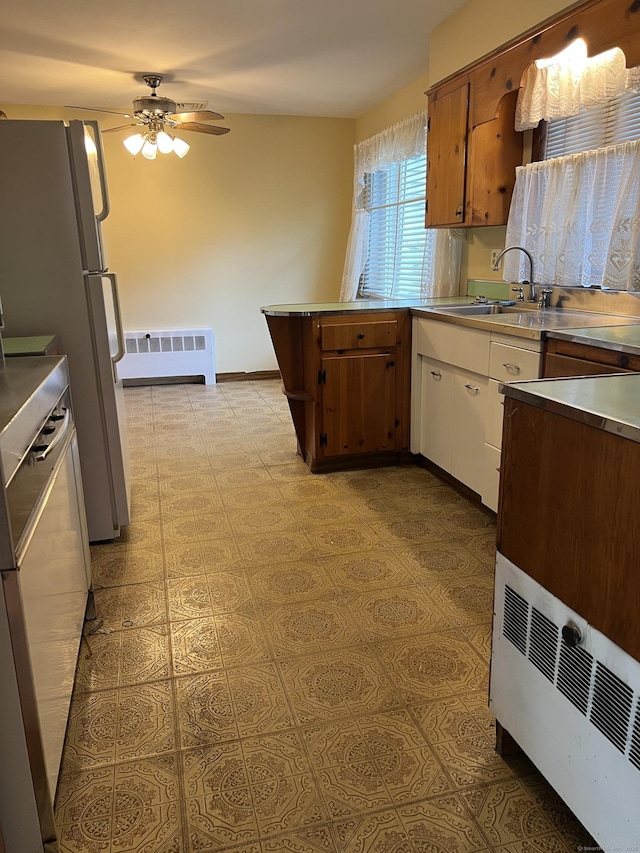 kitchen with stainless steel countertops, ceiling fan, radiator, white cabinetry, and a peninsula