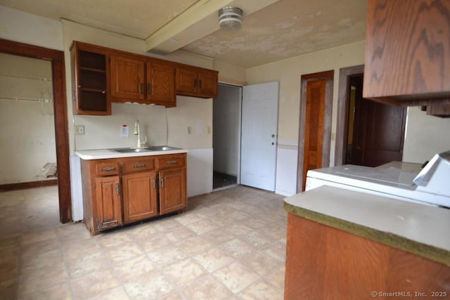 484 W St, Bristol, CT 06010 - kitchen featuring brown cabinetry, light countertops, washer and dryer, light flooring, and beam ceiling