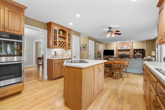 72 Hazelwood Dr, Southington, CT 06489 - kitchen featuring stainless steel double oven, a kitchen island, a ceiling fan, a brick fireplace, and light wood-type flooring