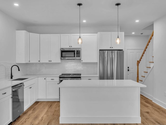 138 Boston Post Rd Unit 15, East Lyme, CT 06333 - kitchen featuring appliances with stainless steel finishes, backsplash, white cabinetry, light wood-style flooring, and a kitchen island