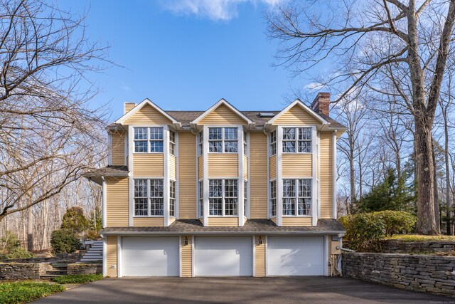 604 W Lake Ave, Guilford, CT 06437 - view of front of property featuring a chimney, driveway, roof mounted solar panels, and a garage