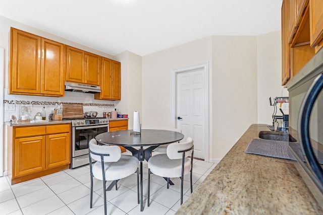 190 Whitney Ave, Bridgeport, CT 06606 - kitchen with under cabinet range hood, stainless steel stove, tasteful backsplash, light tile patterned floors, and brown cabinetry