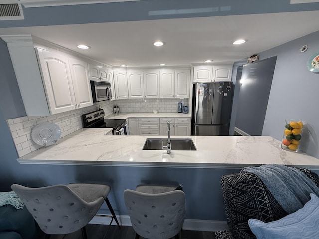3250 Fairfield Ave Apt 100, Bridgeport, CT 06605 - kitchen featuring appliances with stainless steel finishes, a breakfast bar, decorative backsplash, white cabinets, and recessed lighting