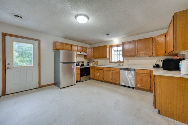 295 Hunting Lodge Rd, Mansfield, CT 06268 - kitchen featuring appliances with stainless steel finishes, under cabinet range hood, brown cabinets, light countertops, and a textured ceiling