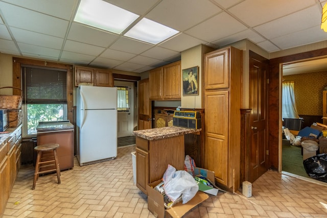 47 Ridge Rd, Middletown, CT 06457 - kitchen with freestanding refrigerator, a drop ceiling, brick flooring, brown cabinets, and a center island