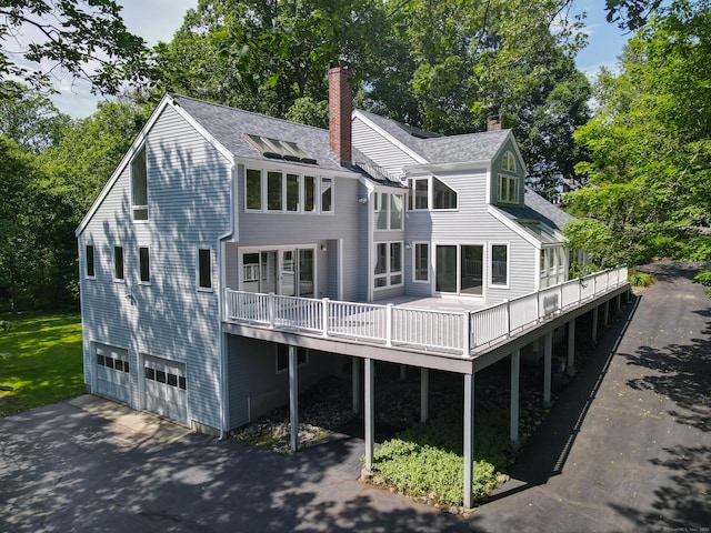 11 Island Bay Cir, Guilford, CT 06437 - rear view of house featuring an attached garage, a chimney, a wooden deck, driveway, and view of scattered trees