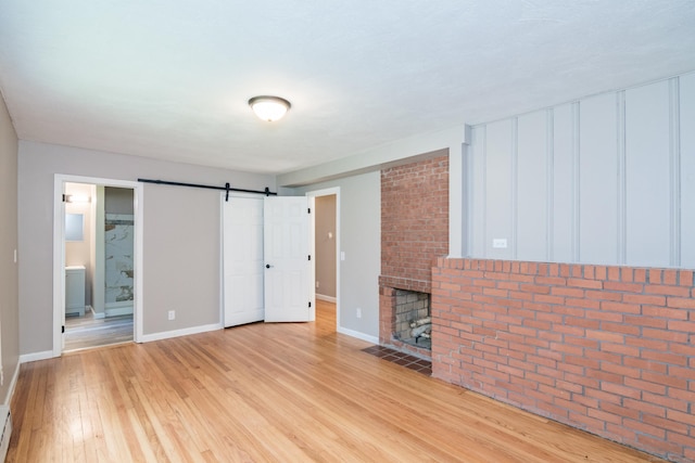 63 Rose Haven Rd, Somers, CT 06071 - unfurnished living room with light wood-style flooring, a barn door, a baseboard radiator, and a brick fireplace