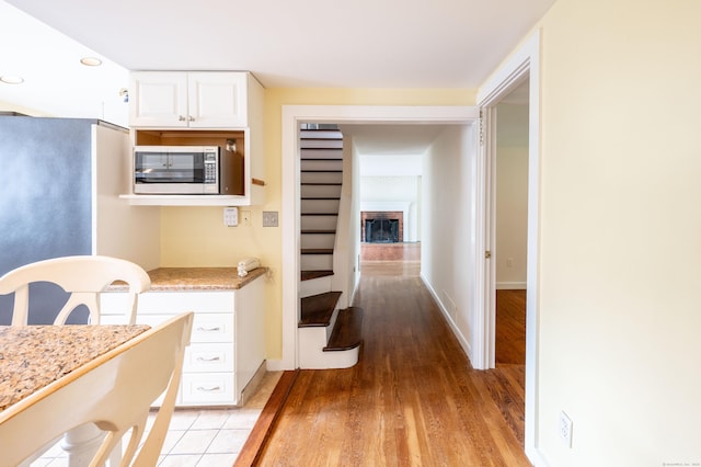 117 Long Meadow Hill Rd, Brookfield, CT 06804 - kitchen with stainless steel microwave, light wood-style flooring, white cabinetry, light stone counters, and a brick fireplace