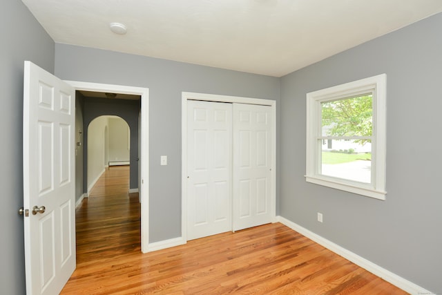129 Tomlinson Ave, Plainville, CT 06062 - unfurnished bedroom with arched walkways, light wood-style flooring, a baseboard heating unit, and a closet
