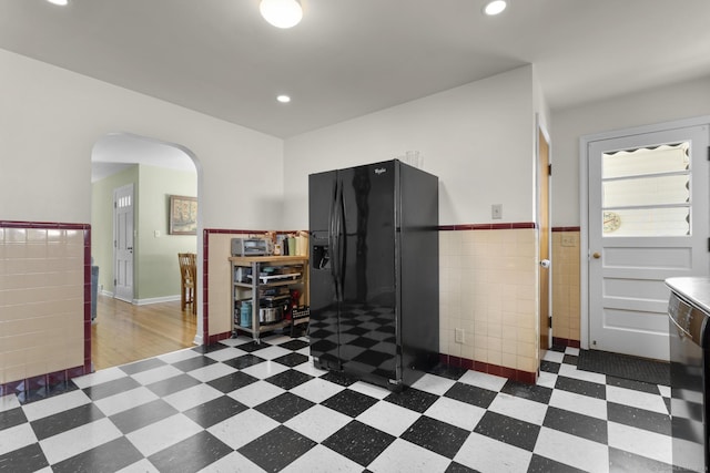 5 Greenfield Dr, Ansonia, CT 06401 - kitchen featuring tile patterned floors, arched walkways, black refrigerator with ice dispenser, tile walls, and wainscoting