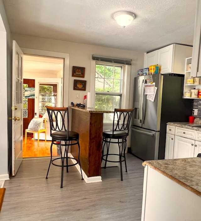 30 Roulin St, Torrington, CT 06790 - kitchen featuring white cabinets, light wood-type flooring, a textured ceiling, freestanding refrigerator, and a breakfast bar