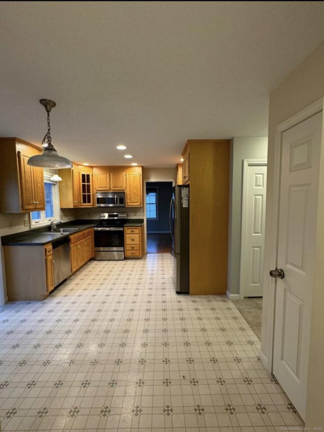 126 Sunnydale Ave, Bristol, CT 06010 - kitchen with appliances with stainless steel finishes, dark countertops, brown cabinetry, pendant lighting, and glass insert cabinets