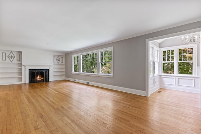 91 Fox Run Rd, New Canaan, CT 06840 - unfurnished living room with light wood-type flooring, built in shelves, a lit fireplace, ornamental molding, and a chandelier