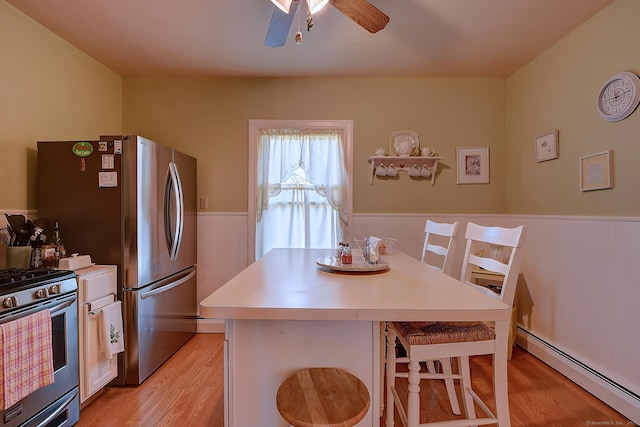 32 Columbus St, East Hartford, CT 06108 - kitchen with a baseboard heating unit, stainless steel gas stove, light wood-style flooring, a breakfast bar area, and wainscoting