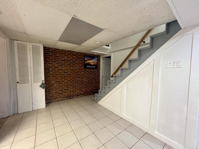 65 Patchen St, Stratford, CT 06615 - finished below grade area with brick wall, a drop ceiling, stairs, and light tile patterned floors