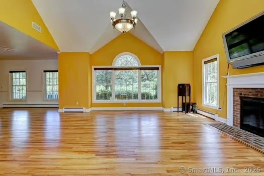 41 Mesa Dr, Bethany, CT 06524 - unfurnished living room featuring wood finished floors, a chandelier, a brick fireplace, lofted ceiling, and healthy amount of natural light