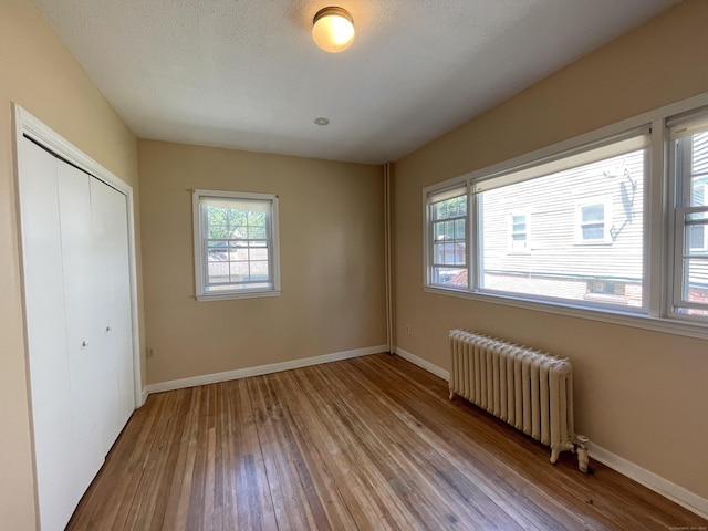 223 S Whitney St, Hartford, CT 06105 - unfurnished bedroom with radiator heating unit, wood-type flooring, and multiple windows