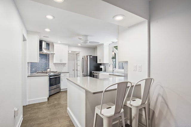 2 Clearview Ave, Norwalk, CT 06851 - kitchen with appliances with stainless steel finishes, wall chimney exhaust hood, a kitchen bar, white cabinetry, and decorative backsplash