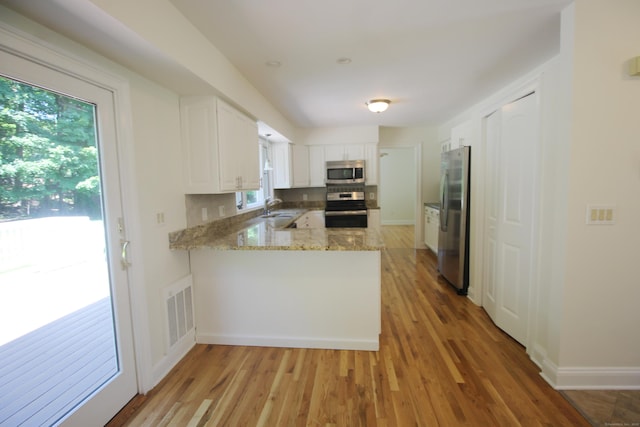 1 Quaker Ridge Rd, Sherman, CT 06784 - kitchen featuring appliances with stainless steel finishes, a peninsula, light wood finished floors, light stone countertops, and white cabinetry