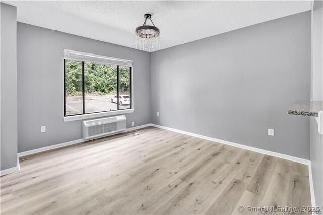 175 Mill Pond Rd Unit 203, Hamden, CT 06514 - unfurnished room featuring a chandelier, wood finished floors, a wall mounted air conditioner, and a textured ceiling