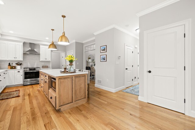 261 W St, Hebron, CT 06248 - kitchen with appliances with stainless steel finishes, wall chimney exhaust hood, white cabinetry, a center island, and light wood-style floors