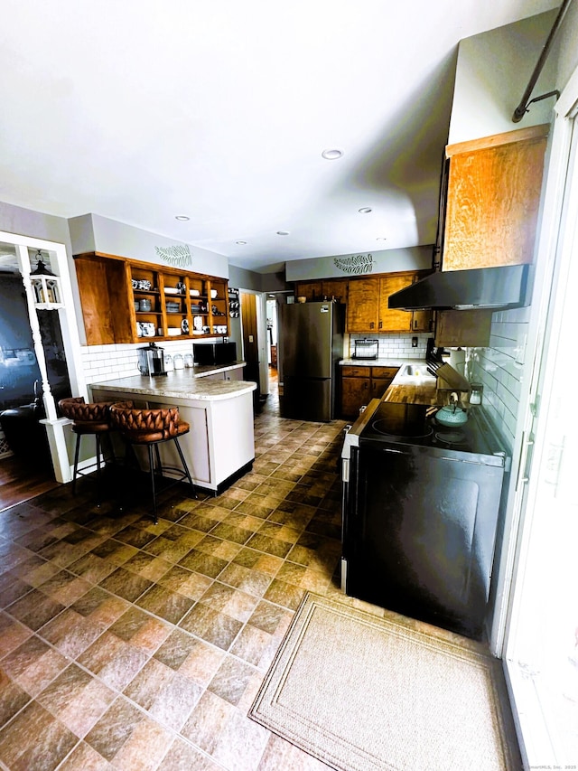 78 French St, Bristol, CT 06010 - kitchen featuring freestanding refrigerator, black / electric stove, a peninsula, decorative backsplash, and a kitchen bar