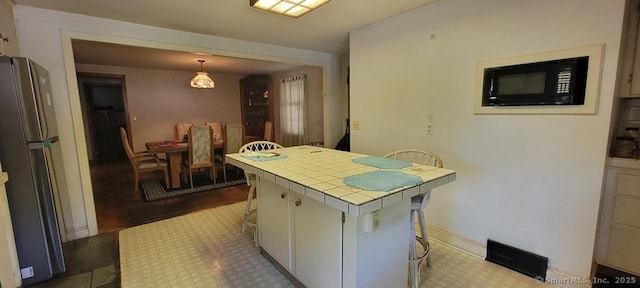 4 Clyne Ave, Waterbury, CT 06705 - kitchen featuring tile countertops, black microwave, freestanding refrigerator, a breakfast bar area, and tile patterned floors