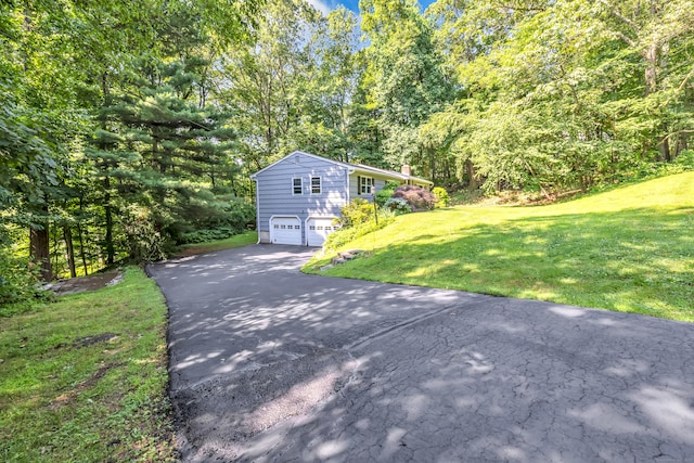 49 Nutmeg Ln, Shelton, CT 06484 - view of side of home featuring asphalt driveway, a garage, a chimney, a lawn, and a view of trees