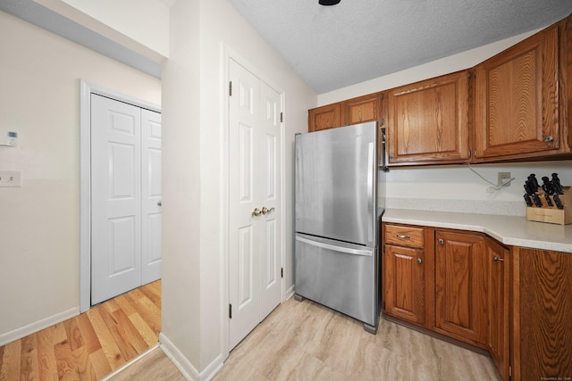 187 Lovers Ln Unit 4, Torrington, CT 06790 - kitchen with freestanding refrigerator, light wood-type flooring, brown cabinetry, light countertops, and a textured ceiling