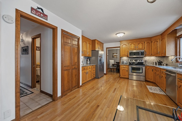 10 Heritage Dr, Prospect, CT 06712 - kitchen featuring appliances with stainless steel finishes, light wood-style floors, brown cabinets, decorative backsplash, and a textured ceiling