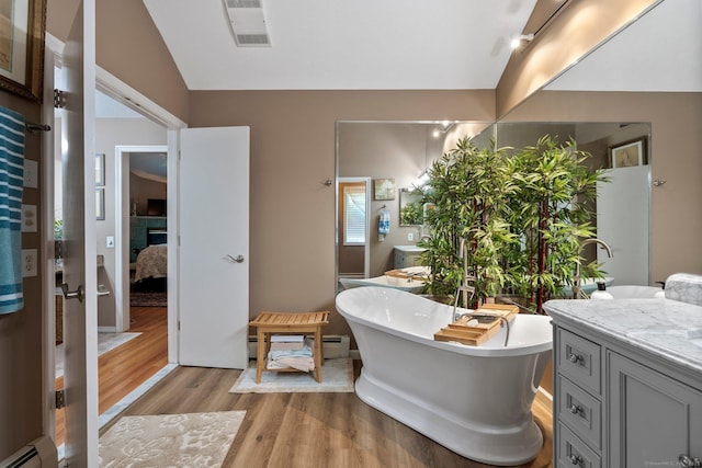 ensuite bathroom with wood finished floors, baseboard heating, lofted ceiling, a soaking tub, and vanity