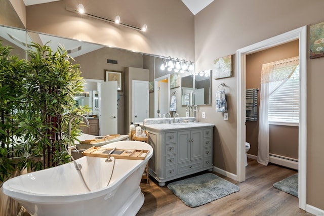 bathroom featuring a baseboard heating unit, a freestanding bath, wood finished floors, vanity, and lofted ceiling