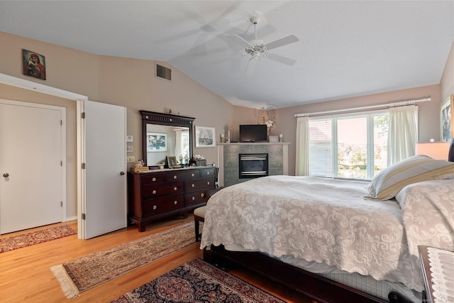 bedroom with wood finished floors, vaulted ceiling, a tile fireplace, and ceiling fan