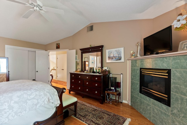 bedroom with wood finished floors, lofted ceiling, a tiled fireplace, a closet, and a ceiling fan
