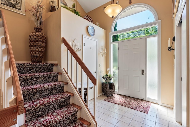 foyer featuring light tile patterned flooring, high vaulted ceiling, and stairs