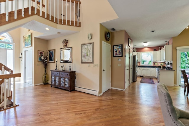 hallway with a baseboard radiator, light wood finished floors, and stairs