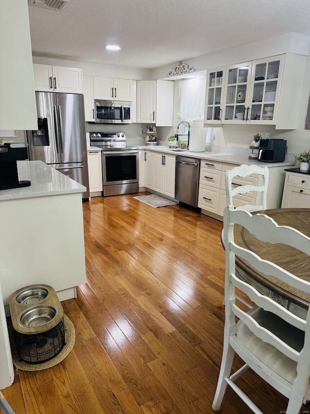 352 Knob Hill Dr, Hamden, CT 06518 - kitchen featuring appliances with stainless steel finishes, white cabinets, glass insert cabinets, and light wood finished floors