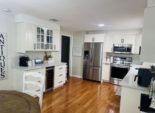 352 Knob Hill Dr, Hamden, CT 06518 - kitchen featuring appliances with stainless steel finishes, wine cooler, glass insert cabinets, wood finished floors, and white cabinets