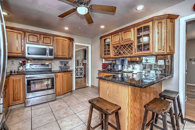 754 Riverside Dr, Orange, CT 06477 - kitchen with appliances with stainless steel finishes, a kitchen breakfast bar, brown cabinetry, tasteful backsplash, and glass insert cabinets