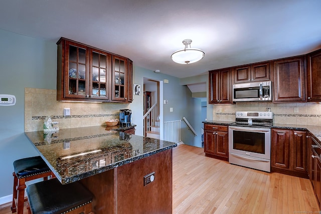 16 Kenwood Rd, Meriden, CT 06450 - kitchen with stainless steel appliances, tasteful backsplash, dark stone countertops, a breakfast bar, and light wood-style floors