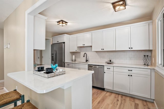 499 Heritage Vlg Unit B, Southbury, CT 06488 - kitchen with appliances with stainless steel finishes, a kitchen breakfast bar, tasteful backsplash, white cabinetry, and light wood finished floors