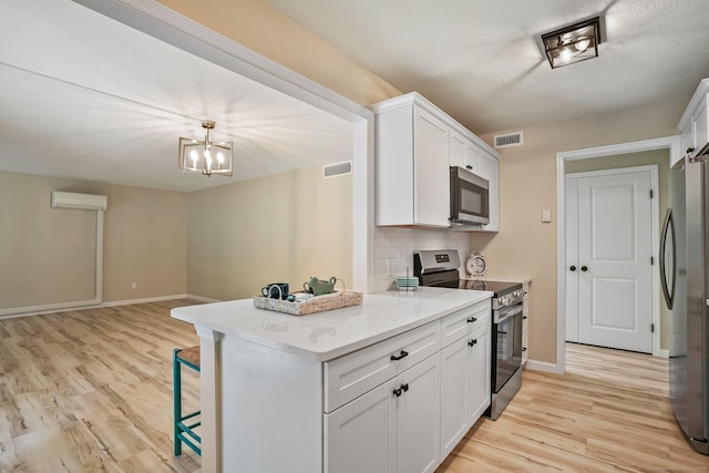 499 Heritage Vlg Unit B, Southbury, CT 06488 - kitchen featuring appliances with stainless steel finishes, light wood-style floors, white cabinets, a wall mounted AC, and a kitchen breakfast bar