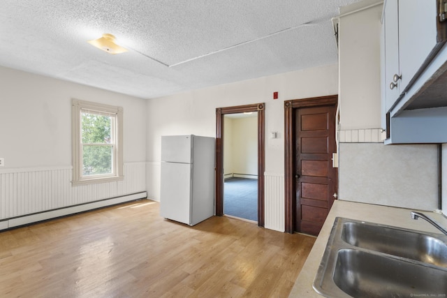 240 Washington St, New Britain, CT 06051 - kitchen featuring freestanding refrigerator, a baseboard radiator, a textured ceiling, a wainscoted wall, and light wood-style floors