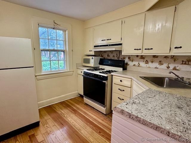 118 Sims St, Bridgeport, CT 06604 - kitchen with white appliances, under cabinet range hood, light wood-type flooring, light countertops, and white cabinetry